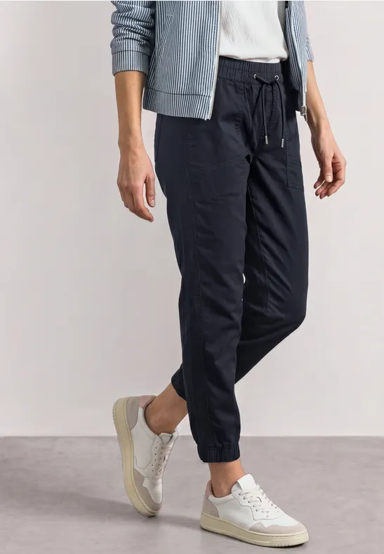Damen-Jogginghose in Schwarz mit Bündchen am Knöchel, kombiniert mit weißen Sneakern und einem hellgrauen Hoodie.