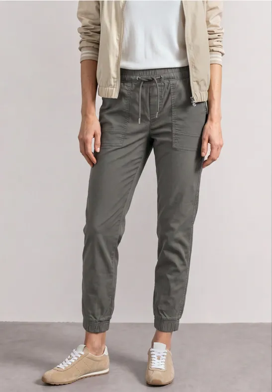 Femme portant chemise blanche, veste claire, pantalon de jogging olive et baskets beiges.