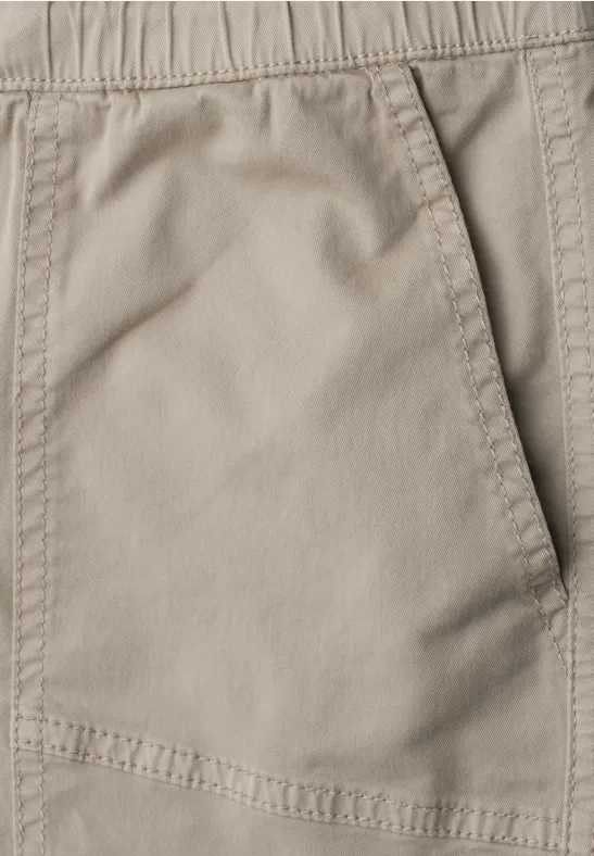 Close-up van een beige broekzak met elastische tailleband en zichtbare stiksels.