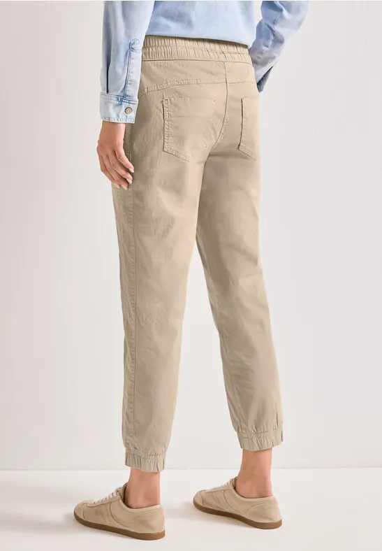 Persoon van achter gefotografeerd draagt lichtbeige chino met elastische enkels en lichtblauw overhemd.