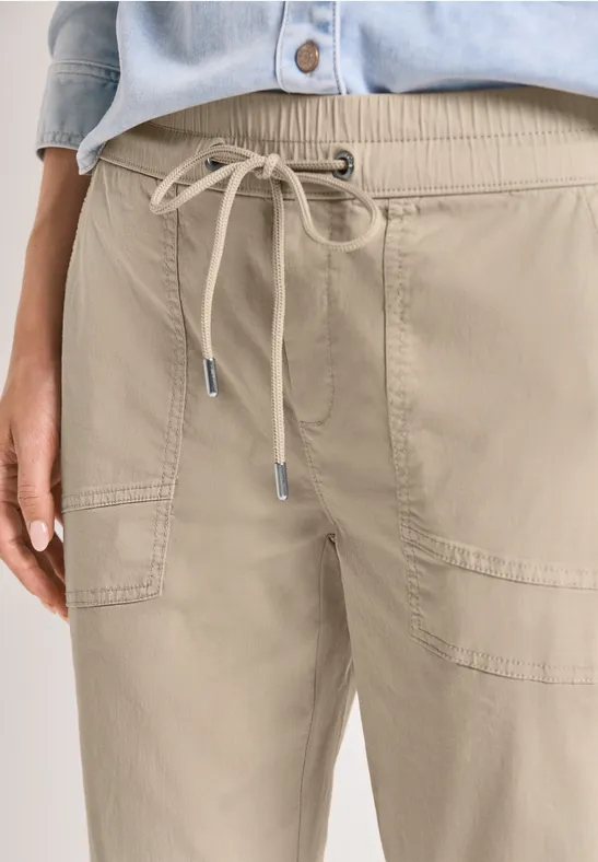 Onderlichaam in beige broek met trekkoord en opgestikte zakken.