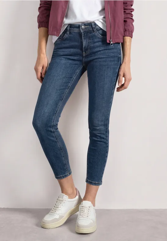 Eine Person trägt schmale blaue Jeans und weiße Sneaker, kombiniert mit weißem Shirt und rosa Cardigan.