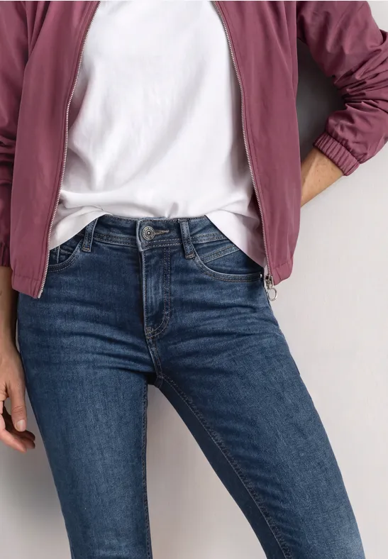 Person trägt blau-enge Jeans, weißes T-Shirt und burgunderrote Jacke