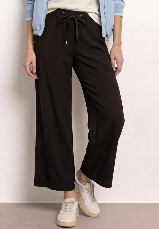 Zwarte, wijde broek met trekkoord in de taille en witte sneakers.