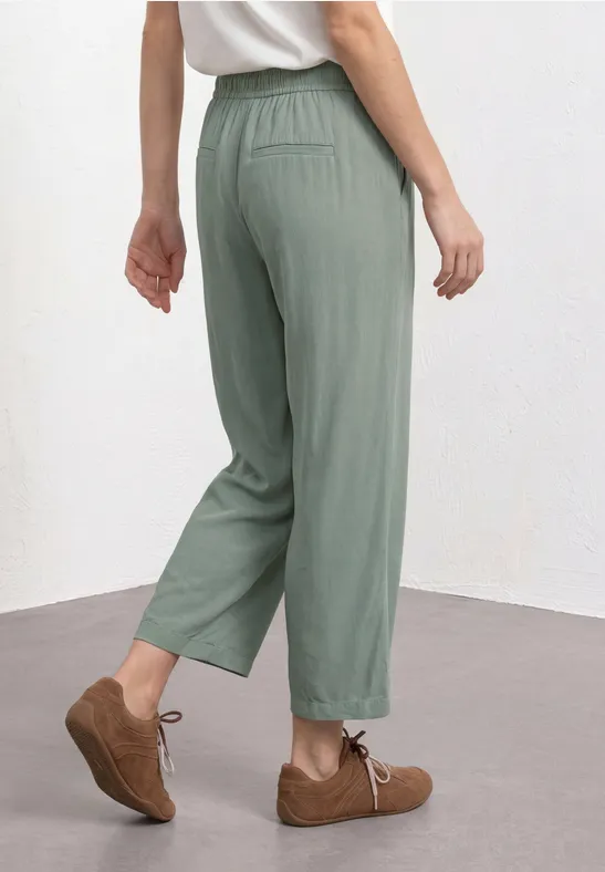 Eine Person trägt locker sitzende, grüne, knöchellange Hose mit elastischem Bund und braune Schnürschuhe.