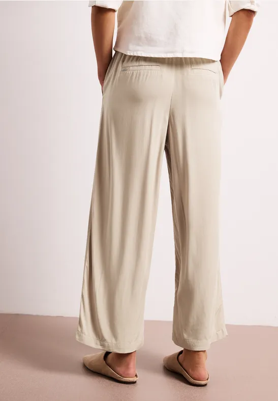 Lichtbeige, wijdvallende broek met elastische taille, losvallende pijpen en subtiele zoom, gecombineerd met sandalen.