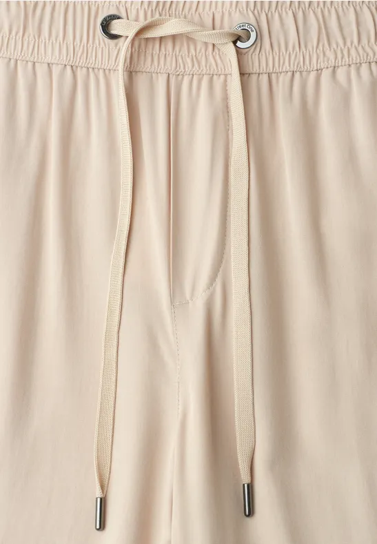 Close-up van een beige broekband met elastische tailleband en koord met metalen oogjes.