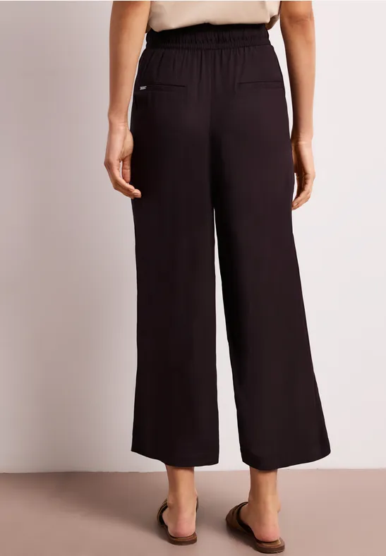 Een vrouw draagt een zwarte, losvallende culotte-broek met elastische taille en zakken.