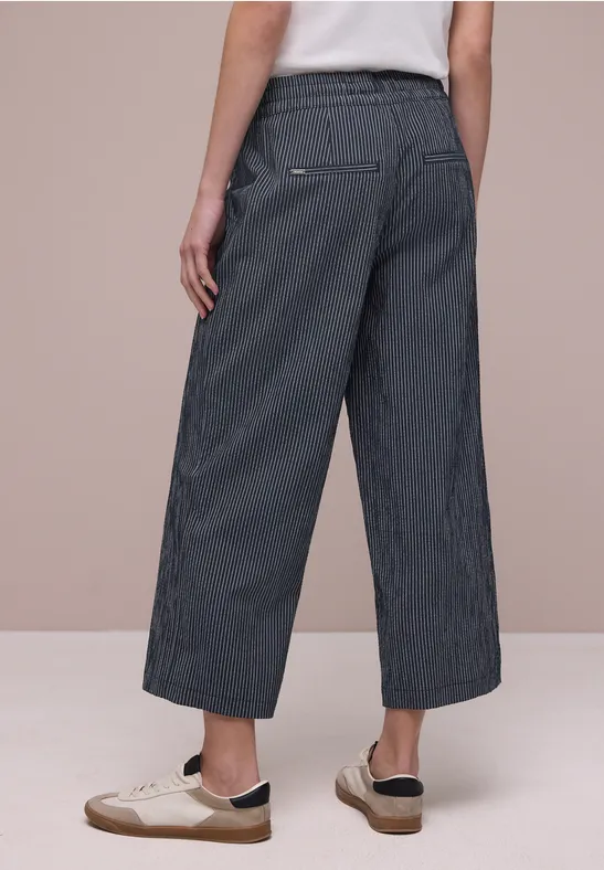 Achteraanzicht: wijd gestreept broekspijpje en witte sneakers voor een beige achtergrond.