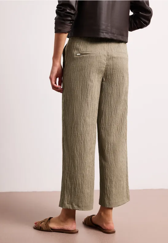 Achteraanzicht van een persoon in losse, geplooide kaki culottebroek en platte sandalen.