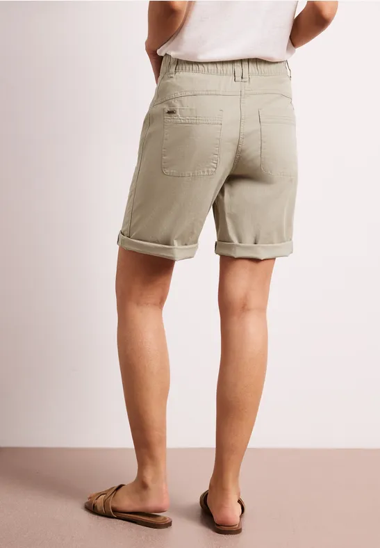 Achteraanzicht van persoon in kaki opgerolde shorts en slippers, lichte achtergrond.