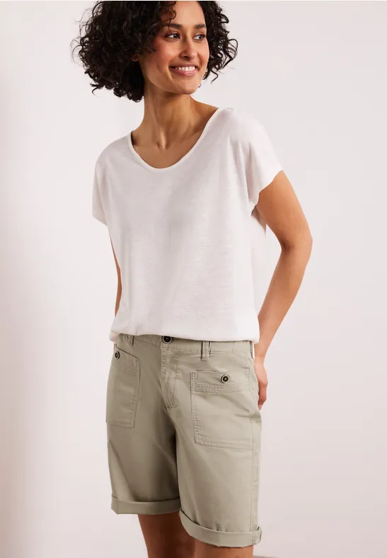 Een persoon draagt een eenvoudig wit T-shirt en beige bermudashort met omslag en zakken.