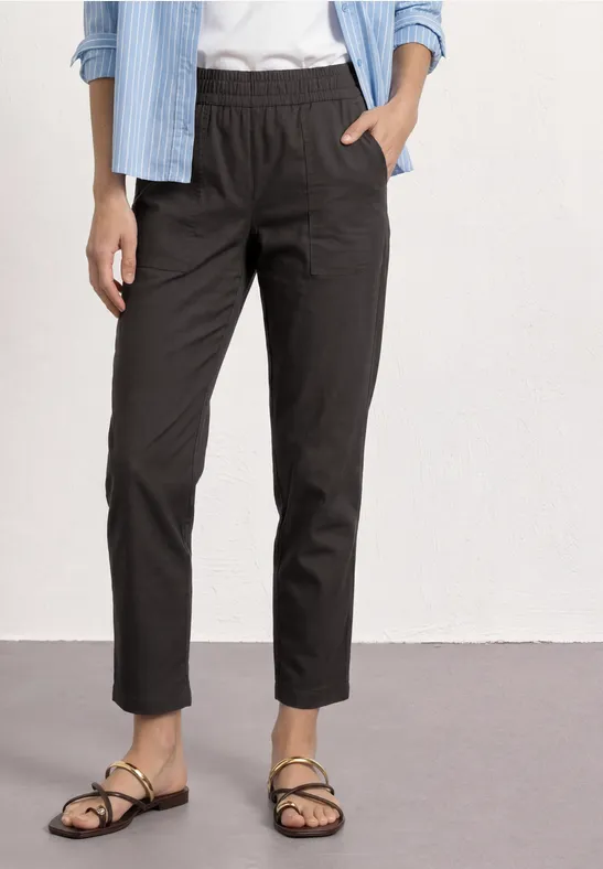 Vrouw draagt zwarte enkellange broek met elastische taille, gecombineerd met wit shirt en sandaaltjes.