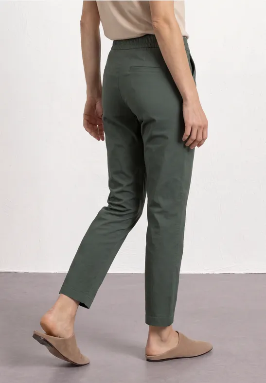 Eine Person trägt grüne, schmale Hose und bequeme braune Mules.