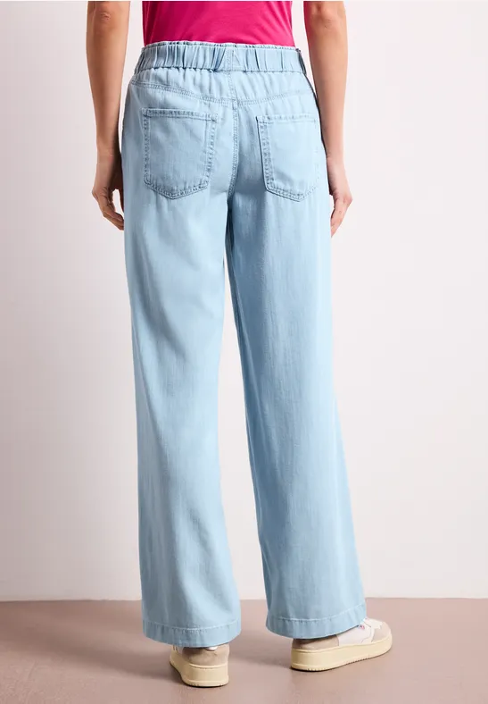 Achteraanzicht van een persoon in lichtblauwe, wijdvallende broek en rood shirt.