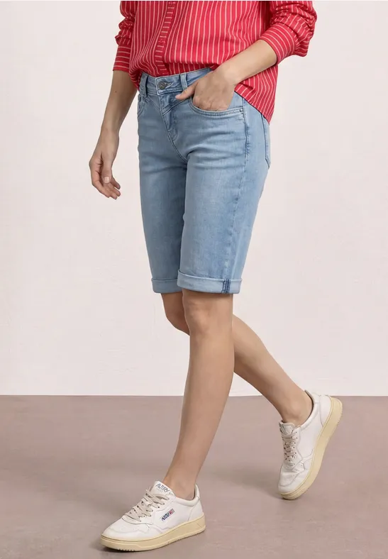 Iemand draagt lichtblauwe denim bermuda met omgeslagen pijpen, witte sneakers en een rood gestreept shirt.