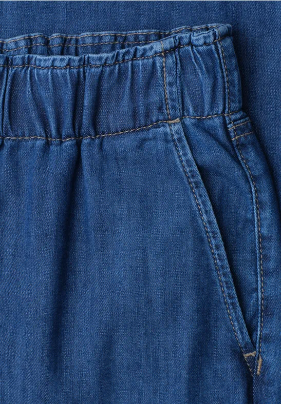 Close-up van een blauwe spijkerbroek met elastische taille en zijzak.