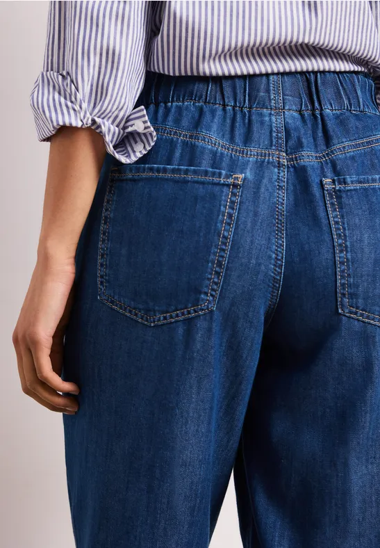 Achteraanzicht van een persoon in blauwe jeans met elastische taille en gestreepte blouse.