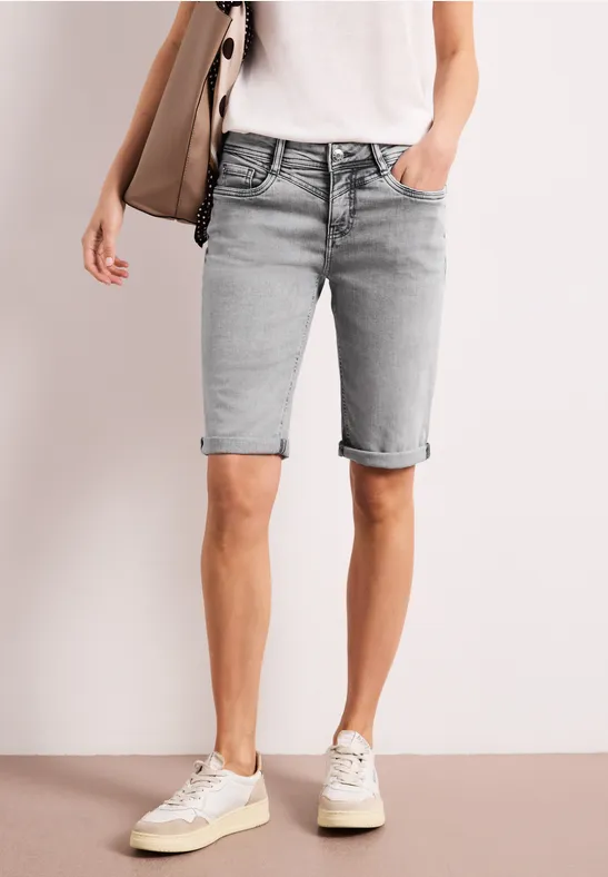 Een persoon draagt lichtgrijze, knielange denim shorts met omgeslagen zoom, gecombineerd met wit T-shirt en sneakers.
