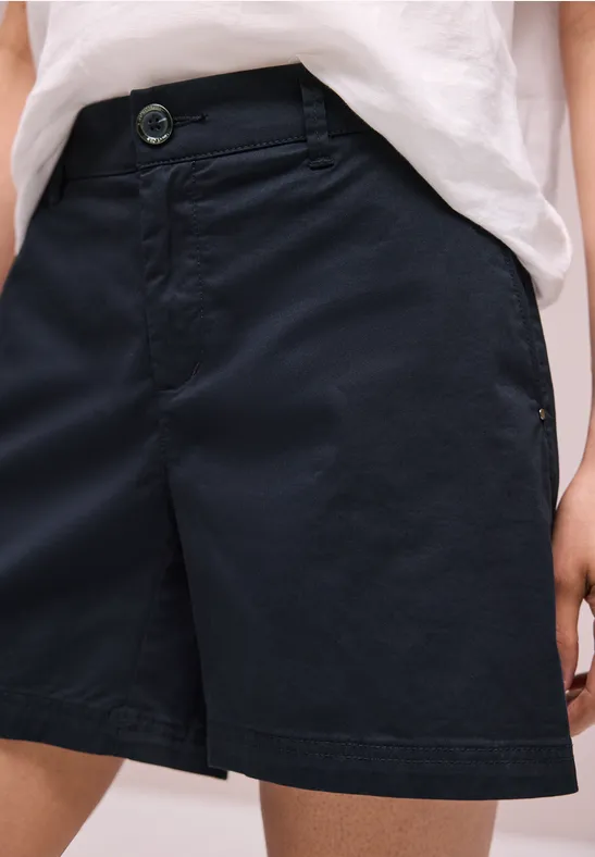 Person trägt dunkelblaue, knielange Shorts mit Knopfverschluss und ein locker eingestecktes weißes T-Shirt.