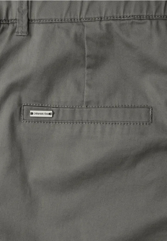 Close-up van een grijze broek met een simpele achterzak en een klein merkje.