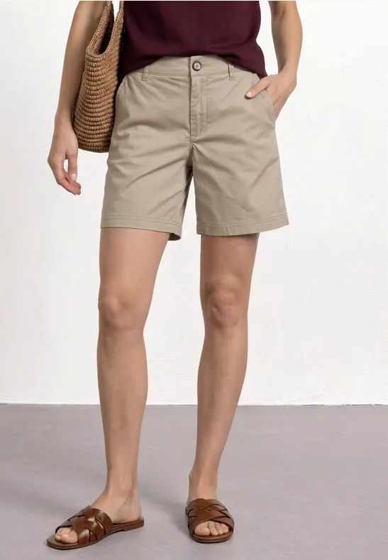 Vrouw met kaki short, bruine sandalen en een rieten tas over de schouder.