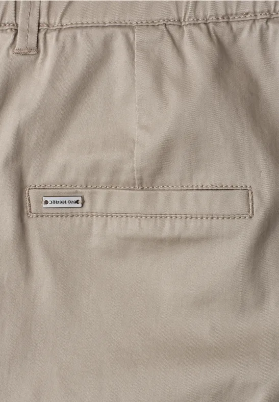 Close-up van een lichtbeige broek met een gesloten achterzak en een klein merkembleem.