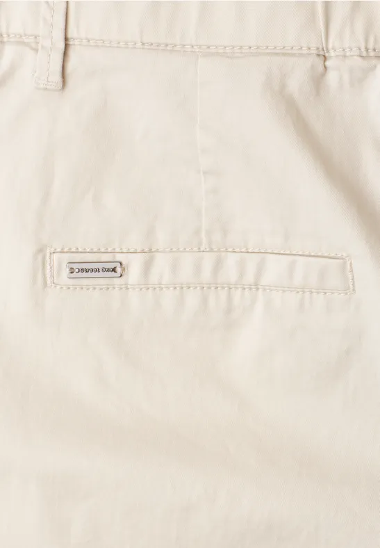 Close-up van een beige broek met een achterzak en klein merkembleem.