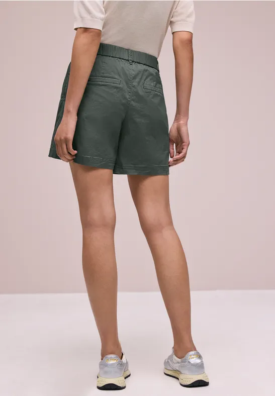 Rückansicht einer Person in schwarzen Shorts, weißem Shirt und Laufschuhen vor neutralem Hintergrund.