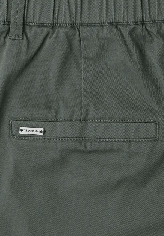 Nahe Ansicht einer olivgrünen Outdoor-Hose mit Reißverschlusstasche und Label am Bund.