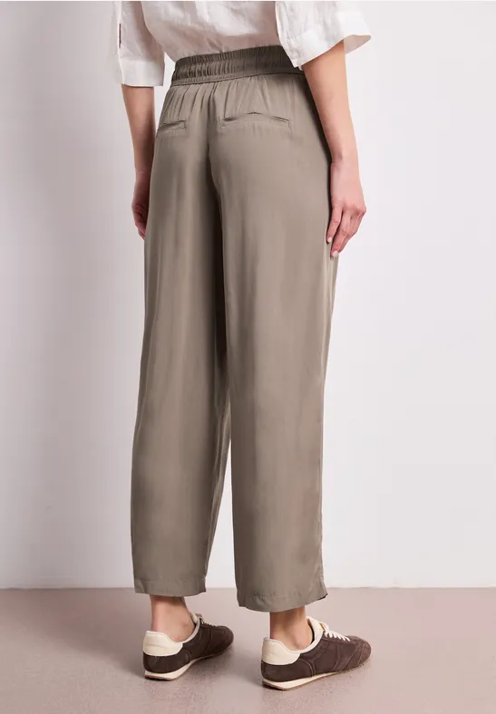 Rückansicht einer Person mit locker sitzender, olivgrüner, knöchellanger Hose und schlichten Schuhen.