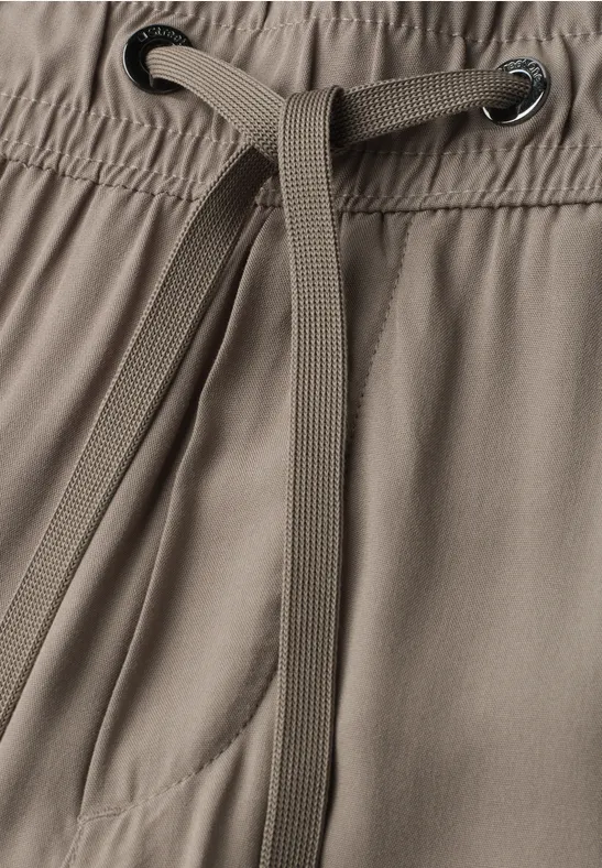 Nahaufnahme eines Tunnelzugs und Bunds einer graubraunen Hose mit Tasche