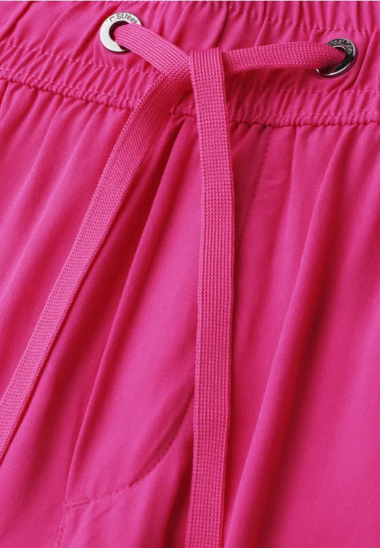 Nahaufnahme eines pinken Kleidungsstücks mit elastischem Bund und pinker Kordel durch Metallösen.