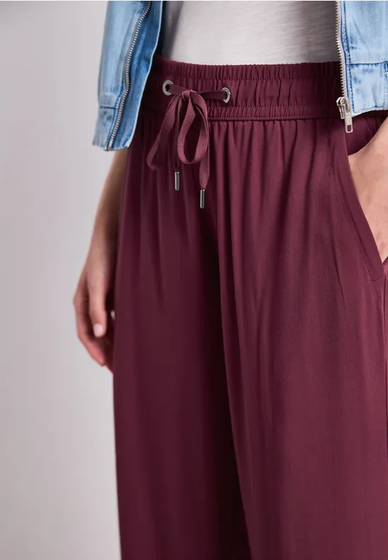 Lässige, bordeauxrote Hose mit Tunnelzug und Einschubtaschen, kombiniert mit weißem Top und Jeansjacke.