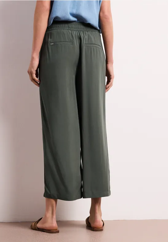 Achteraanzicht van een persoon met olijfgroene, wijde culottebroek en platte sandalen.