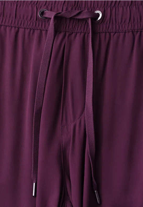 Close-up van de taille van een bordeauxrode broek met elastische band en aantrekkoord.