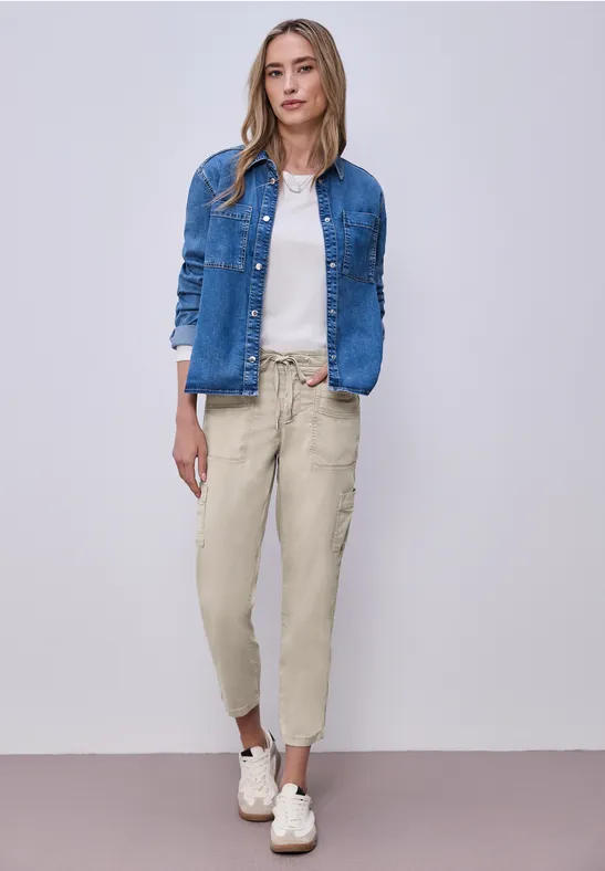 Eine Frau in Jeansjacke, weißem Shirt, beigen Cargohosen und weißen Sneakern.