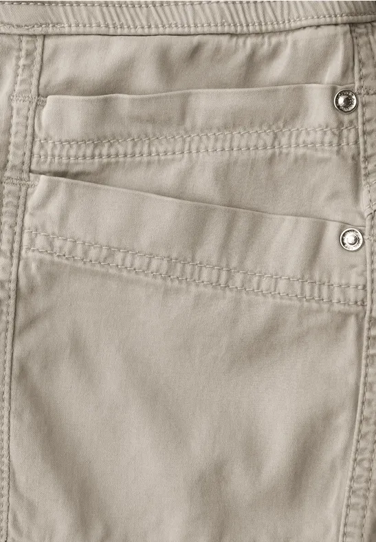 Nahaufnahme einer beigen Hose mit mehreren Taschen und sichtbaren Nähten sowie Druckknöpfen.
