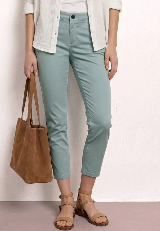 Iemand draagt mintgroene chino, sandalen en een bruine suède leren tas.