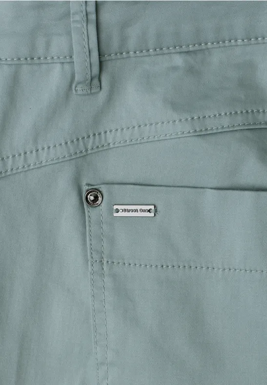 Close-up van een lichtgroene broek met zijzak en klein label.