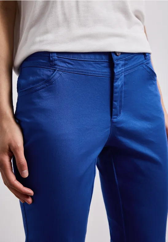 Een persoon draagt een felblauwe chino en een wit shirt, alleen het onderste deel van de romp is zichtbaar.