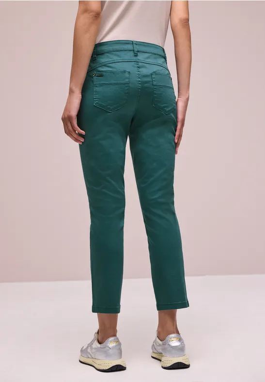 Person von hinten, trägt grüne Hose und weiße Sneaker vor schlichter Kulisse.