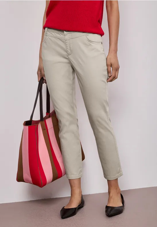 Frau trägt rote Bluse, beige Chinohose, schwarze Ballerinas und gestreifte rote-rosa Tragetasche.