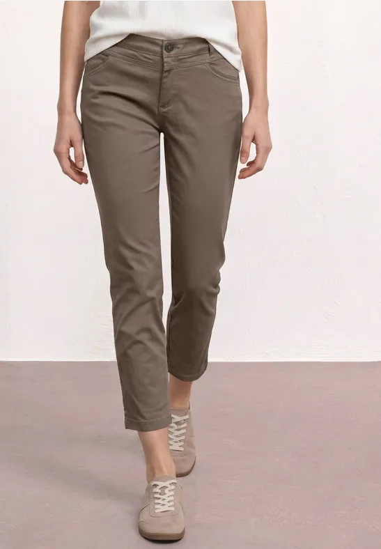 Vrouwelijk model draagt kaki chino en lichte sneakers voor witte achtergrond.