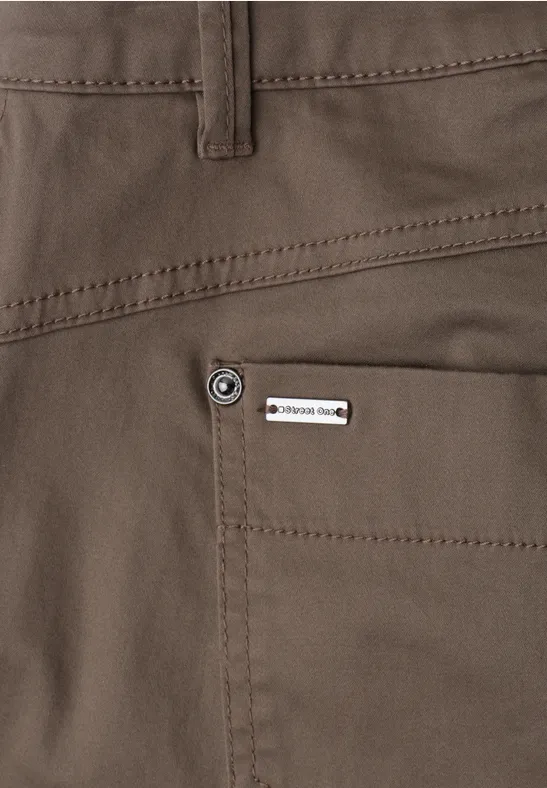 Close-up van een donkerbruine broek met achterzak en klein metalen label.