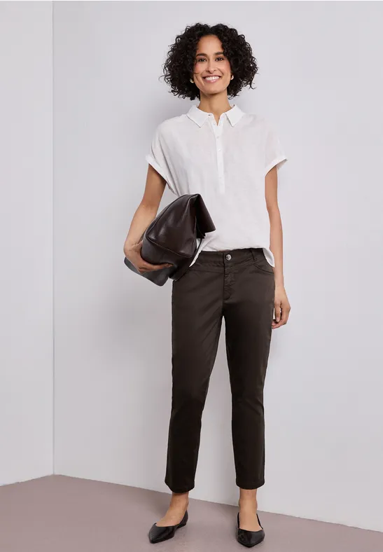 Frau trägt weiße Bluse, schwarze Hose, schwarze Ballerinas und hält schwarze Clutch.