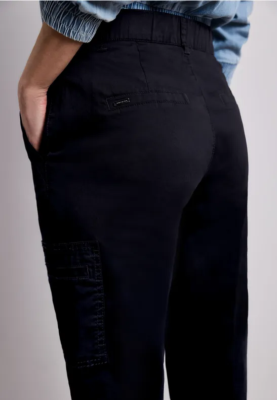 Person von hinten in schwarzer Hose mit seitlicher Tasche, Hände in den Taschen sichtbar.