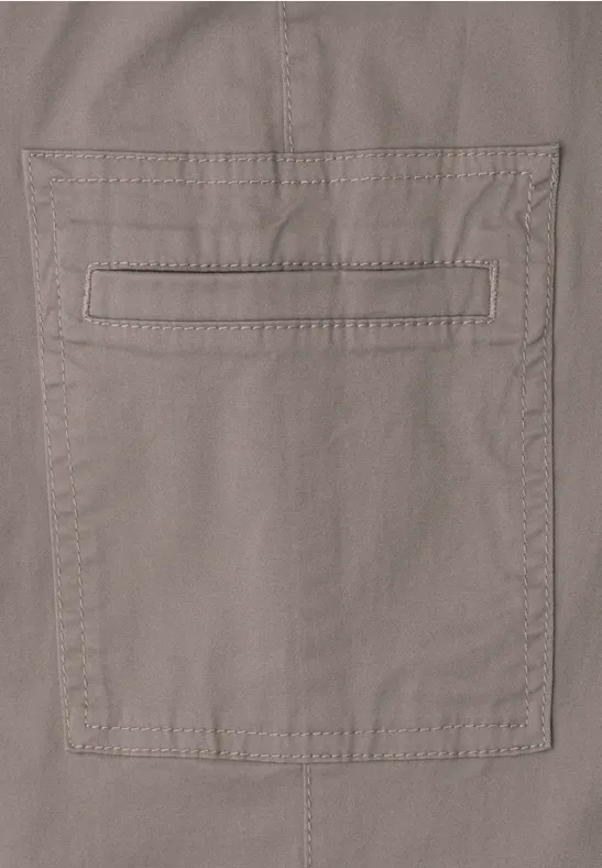 Nahe Ansicht einer beigen Stoffhose mit aufgesetzter Tasche und feinen Ziernähten.