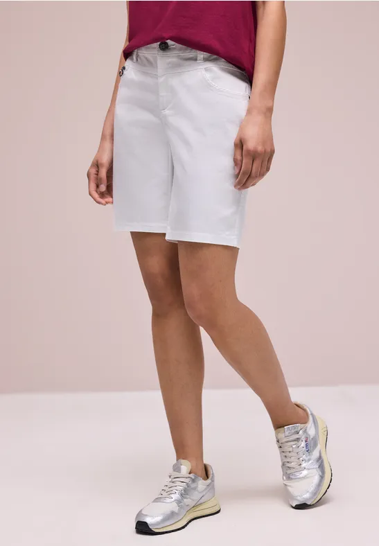 Frau trägt rotes Shirt, weiße Jeans-Shorts und silberne Sneaker.