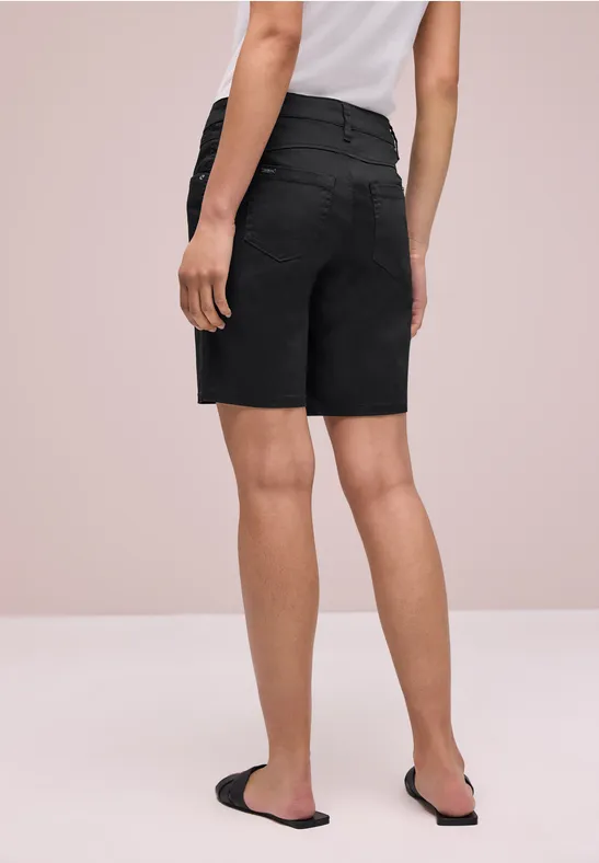 Achteraanzicht van een persoon in zwarte bermudashorts, een wit T-shirt en zwarte sandalen tegen een lichte achtergrond.